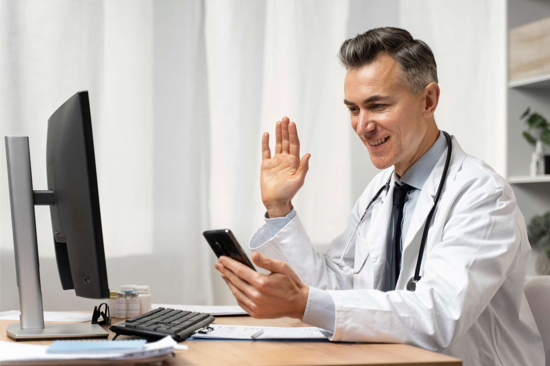 Arzt mit Smartphone am Computer